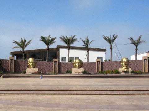 1986 Ford Bronco - A person walks past a row of large golden busts in an outdoor plaza with palm trees and a modern building.
