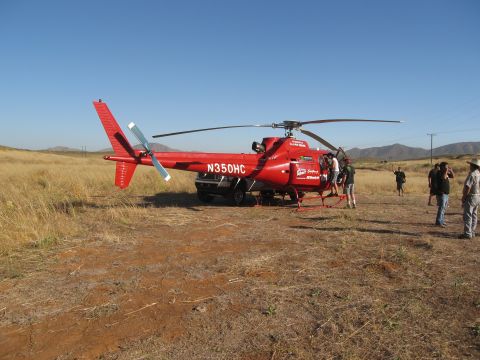 1986 Ford Bronco - A red helicopter, identified by the registration N350HC, sits on the ground in a rural, arid landscape with several people nearby.