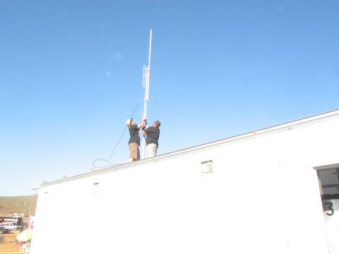 1986 Ford Bronco - Workers install a tall antenna on the roof of a building under a clear blue sky.
