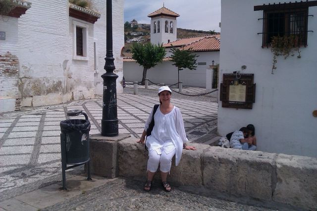 Woman in white sitting on a stone wall in a European town square with a tower in the background