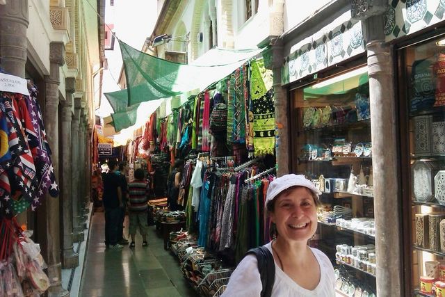 Woman smiling in a narrow market street lined with stalls selling textiles and crafts