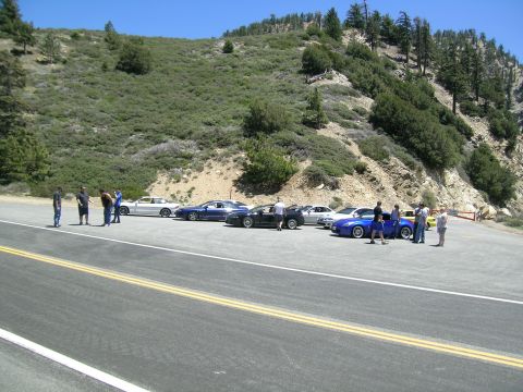 1993 Ford Probe - A group of cars are parked on the side of a mountain road, with several people gathered around.