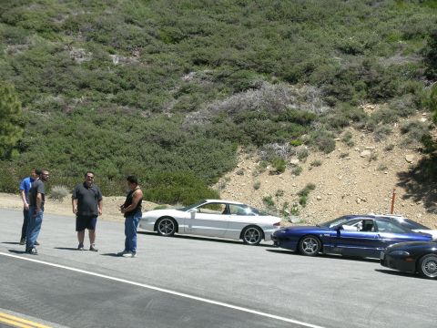 1993 Ford Probe - Several people stand near a line of parked cars, including a white 1993 Ford Probe, on a sunny day.