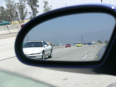 1993 Ford Probe - View of a white 1993 Ford Probe from a side mirror while driving on a multi-lane highway.
