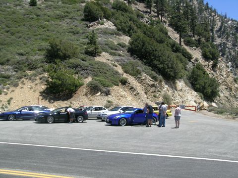 1993 Ford Probe - A group of cars are parked on a scenic mountain road, with people gathered around some of them.