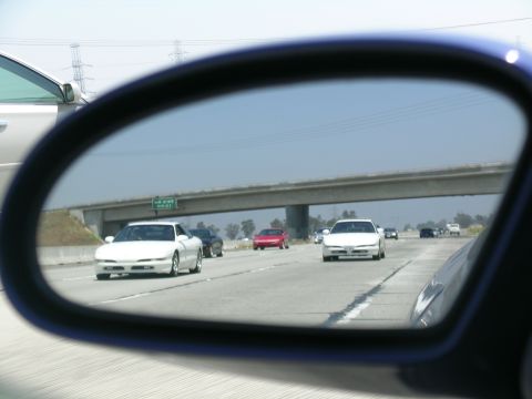 1993 Ford Probe - A white 1993 Ford Probe is seen in the side mirror while driving on a highway, with other vehicles also present.