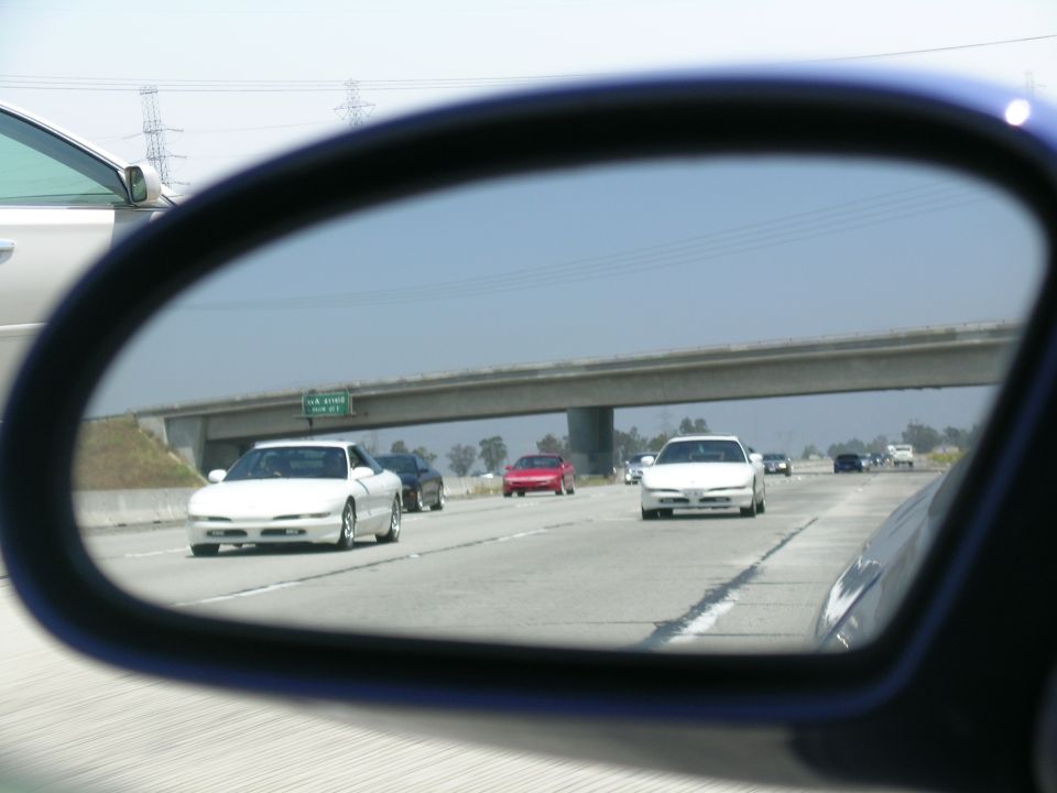 White 1993 Ford Probe seen from side mirror on highway