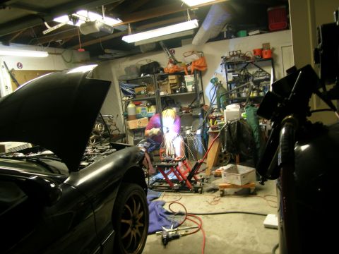 1995 Ford Probe - A person welds in a cluttered garage next to a black car with its hood open.