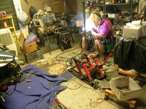 1995 Ford Probe - A person is welding in a workshop with various machinery and supplies scattered around.