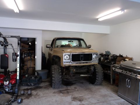 1990 Chevrolet Suburban - A lifted pickup truck is parked inside a garage next to a weight rack and a grill.
