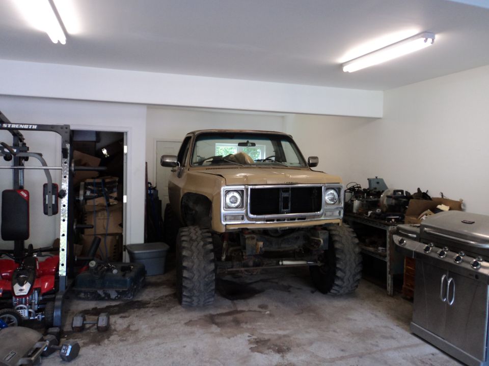 Lifted tan pickup truck with large tires parked in a garage, front view