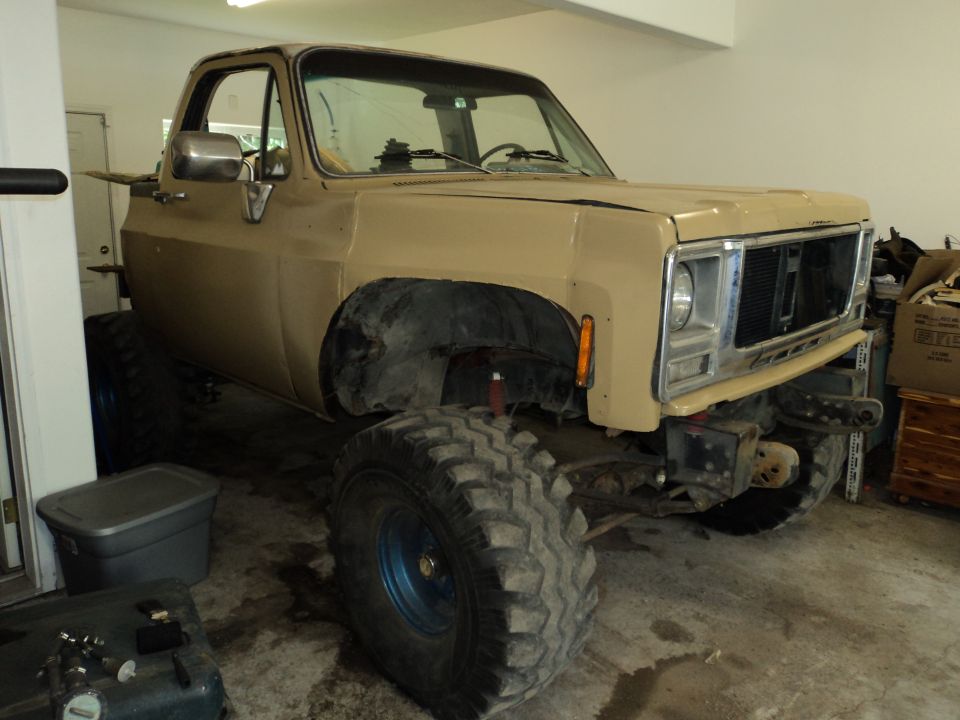 Tan pickup truck with large off-road tires, lifted suspension, and a missing grille