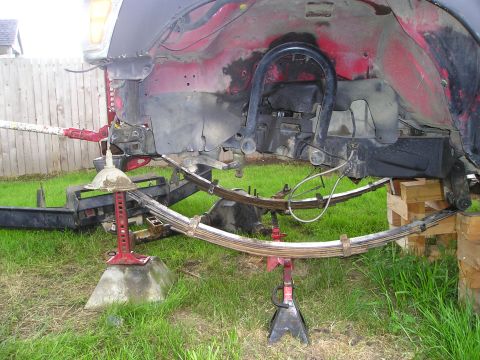 1990 Toyota Pickup/SR5 - The rear suspension of a red truck, leaf springs supported by jacks and wooden blocks.