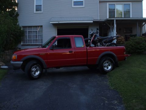 1997 Ford Ranger - A red pickup truck is parked in a driveway, carrying a dirt bike in its bed.