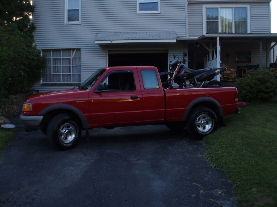 Red pickup truck parked in driveway with a dirt bike in the bed. House in background