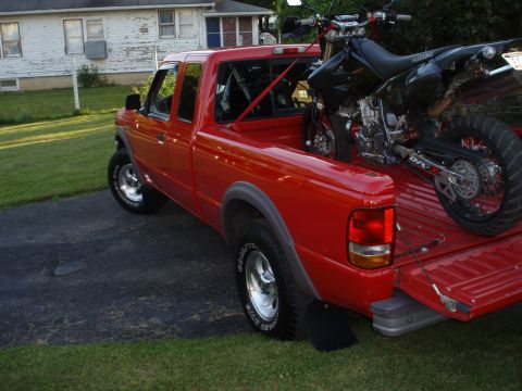 1997 Ford Ranger - A red 1997 Ford Ranger pickup truck is shown from a three-quarter front angle, with a motorcycle loaded in its bed.