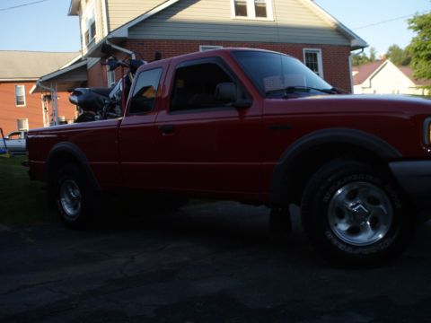 1997 Ford Ranger - A red pickup truck is parked in a driveway with a motorcycle loaded in the bed.