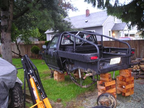 1990 Toyota Pickup/SR5 - A black pickup truck is elevated on wooden blocks, showing its suspension and custom rear end.