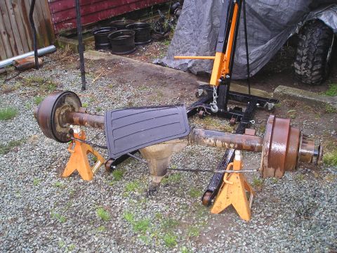 1990 Toyota Pickup/SR5 - A rusty rear axle assembly is supported by orange jack stands outdoors.