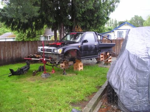 1990 Toyota Pickup/SR5 - A black 1990 Toyota Pickup/SR5 is shown with its front end disassembled and raised on jacks in a yard.