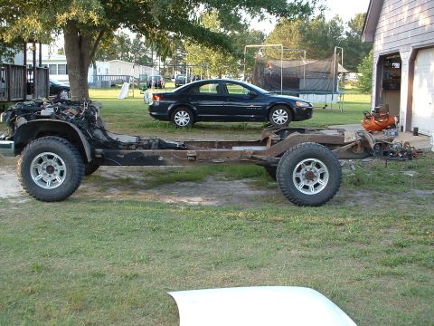 1994 GMC Suburban - Vehicle frame and engine assembly outdoors, with a sedan in the background.
