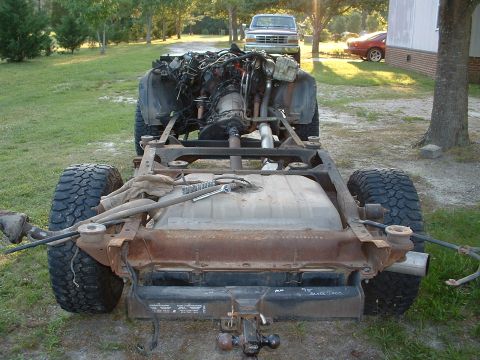 1994 GMC Suburban - The chassis of a vehicle is shown with its engine and fuel tank exposed, with other vehicles in the background.