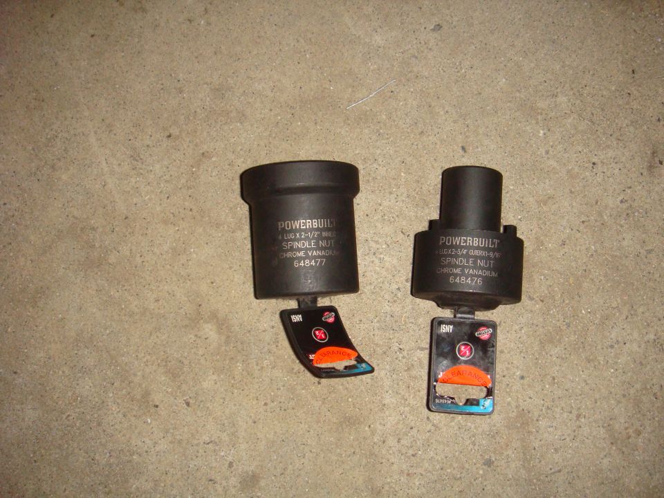 Two black Powerbuilt spindle nut sockets with orange and blue tags on a concrete surface