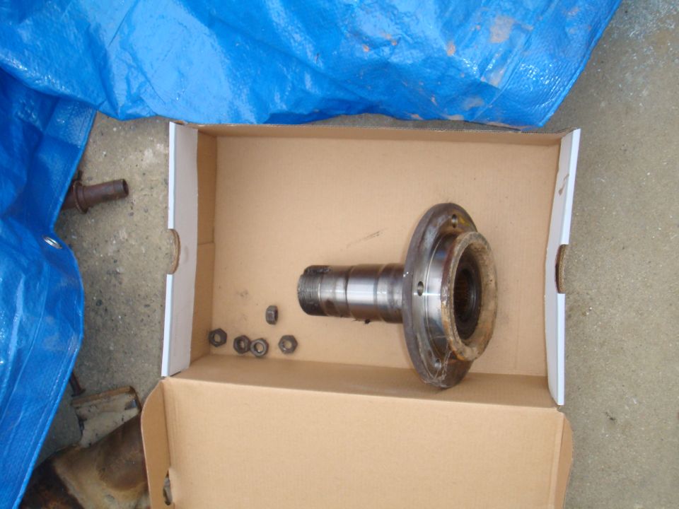 Vehicle axle part and nuts in a cardboard box, under a blue tarp