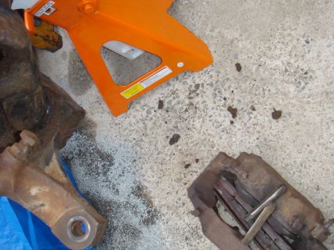 1992 Ford Bronco - Vehicle axle parts and orange jack stands are laid out on a concrete surface, with some debris scattered around.