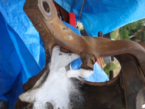 1992 Ford Bronco - A close-up of a rusty vehicle suspension part being cleaned with soap and water.