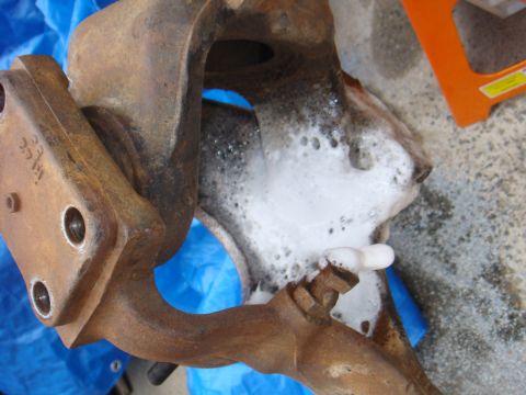 1992 Ford Bronco - A close-up view of a rusty metal component, possibly a suspension part, being cleaned with soap and water.