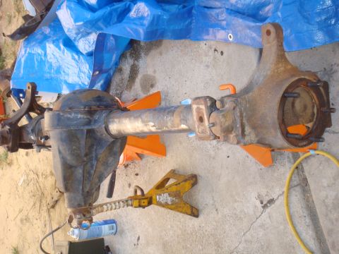 1992 Ford Bronco - A disassembled rear axle assembly rests on jack stands, partially covered by a blue tarp.