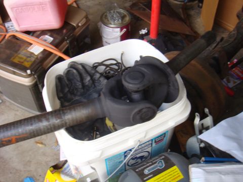 1992 Ford Bronco - A driveshaft and U-joint are stored in a bucket with a pair of black gloves.
