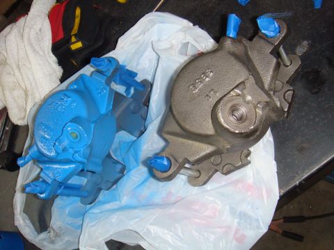 1992 Ford Bronco - Two brake calipers, one painted blue and the other in gray, are placed on a plastic bag, ready for installation or after a rebuild.