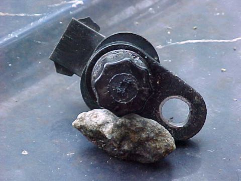 1995 Ford Bronco - A detached automotive part rests on a textured surface next to a small rock.