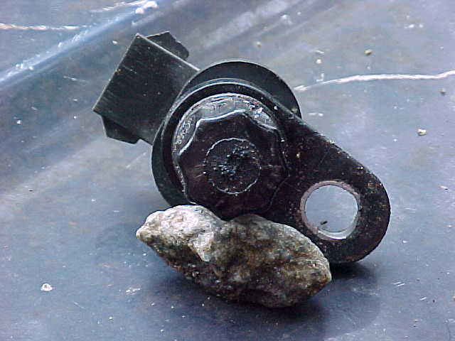 Bottom of a small black sensor with hex bolt and mounting ear, propped on a rock