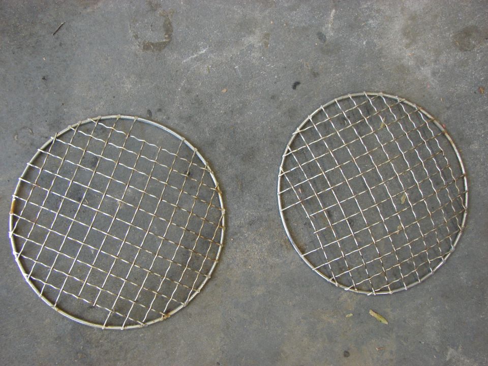 two round metal grilles with wire mesh, lying on a concrete surface