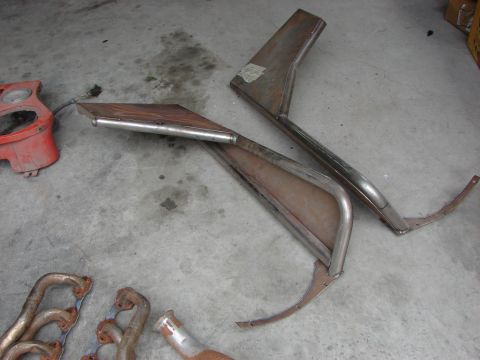 1978 Ford Bronco - Various automotive parts, including exhaust manifolds and metal fender sections, are laid out on a concrete floor.