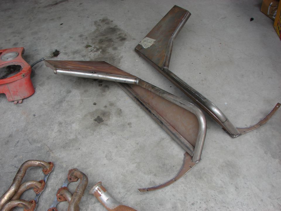 Car parts including exhaust manifolds and fender sections on concrete