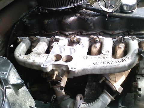 1981 Ford Bronco - Close-up of a cast-aluminum Offenhauser Dual-Port intake manifold bolted to an inline-six engine with a blackened valve cover, its carburet…