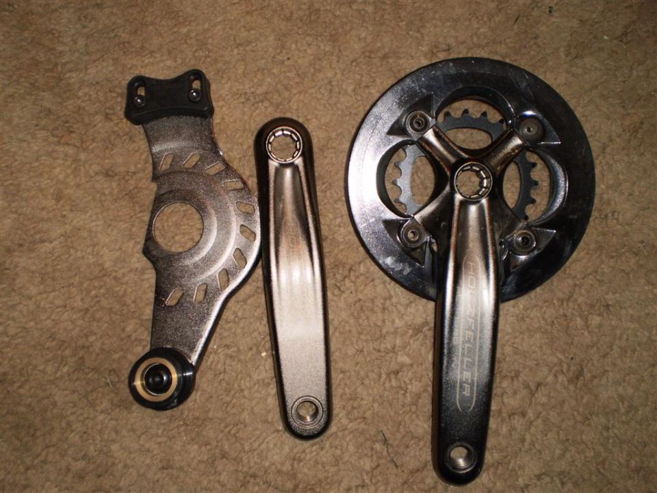 Bike crankset, chainring, and chain guard laid out on carpet