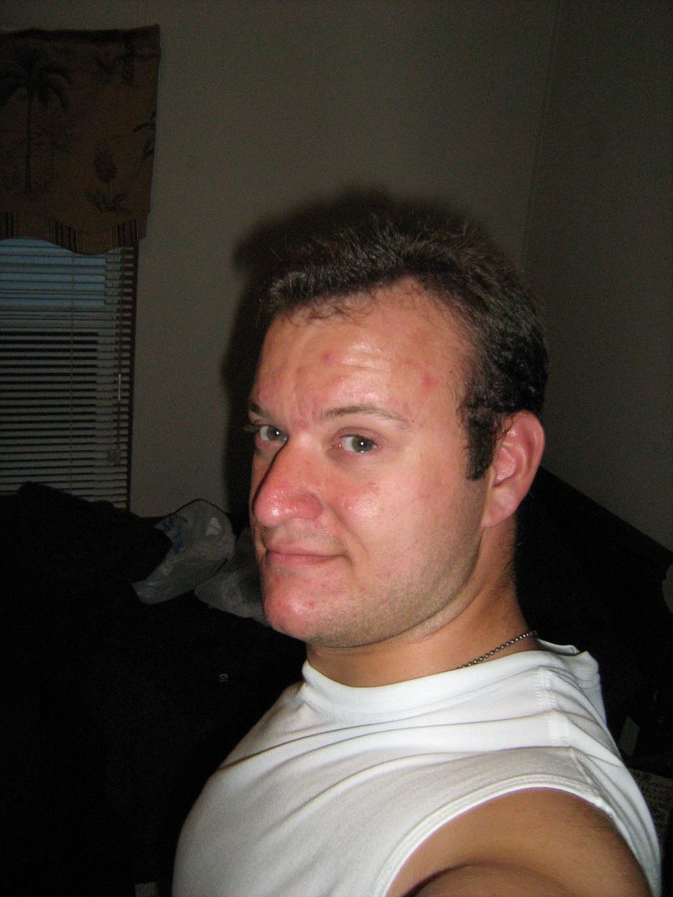 Young man in a white tank top taking an indoor selfie