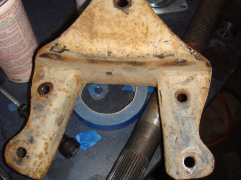 1992 Ford Bronco - A heavily rusted metal bracket with visible bolt holes sits on a workbench next to a splined shaft.