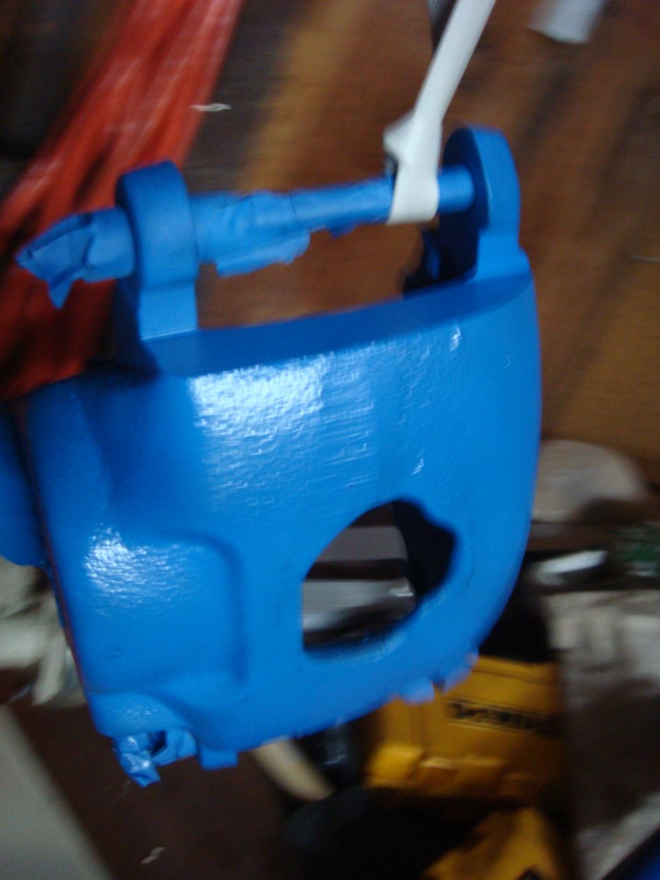 Blue painted brake caliper with tape on it, hanging by a strap. Supermotors.net logo visible