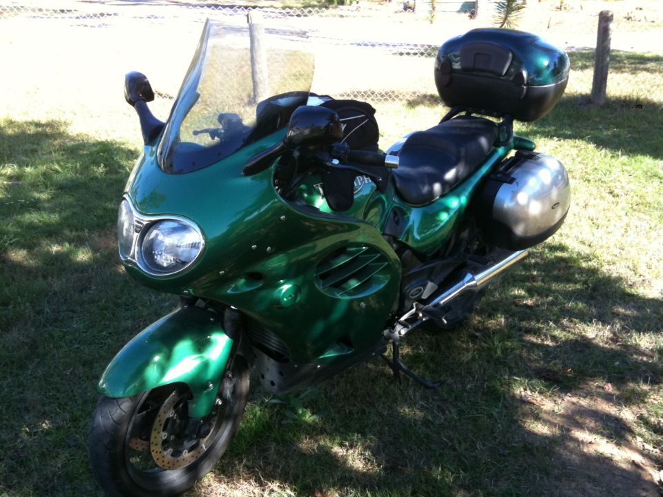 Green touring motorcycle with saddlebags and a top case parked on grass