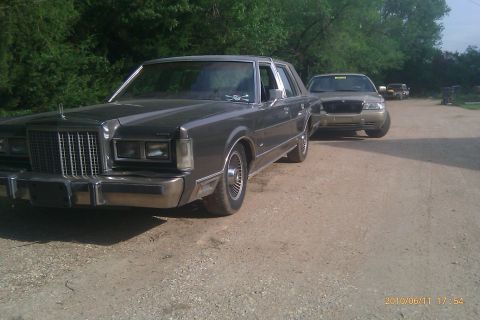 2000 Mercury Grand Marquis - Two sedans are parked on a dirt road, with trees lining the background.