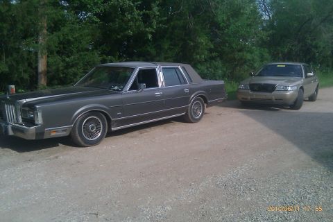 2000 Mercury Grand Marquis - Gold sedan parked on a gravel road, with a Lincoln Town Car in the foreground. The gold sedan appears to be a 1998 model.