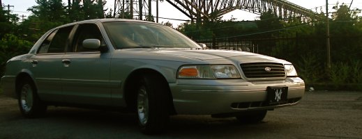 Silver sedan parked outside with a bridge in the background. Has a New York Yankees license plate frame
