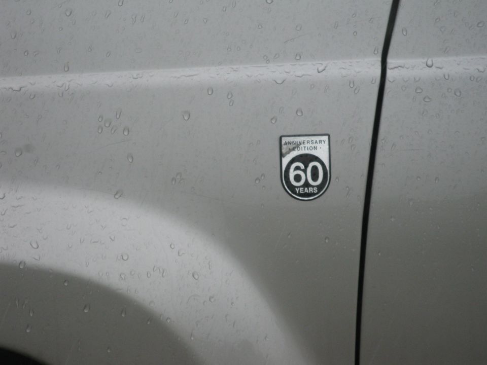Silver vehicle fender with a "60 Years Anniversary Edition" badge, water droplets on surface