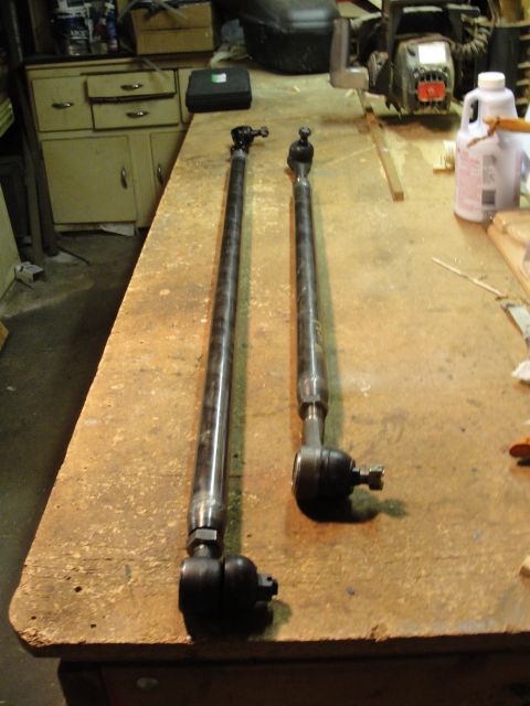 1995 Ford Bronco - Two metal tie rods with ball joints are laid out on a wooden workbench, possibly for a vehicle modification project.